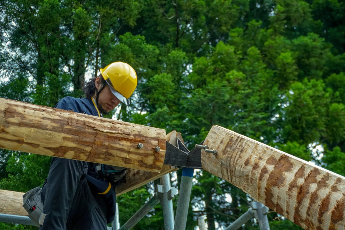 作業員が丸太の梁を組み立てる様子
