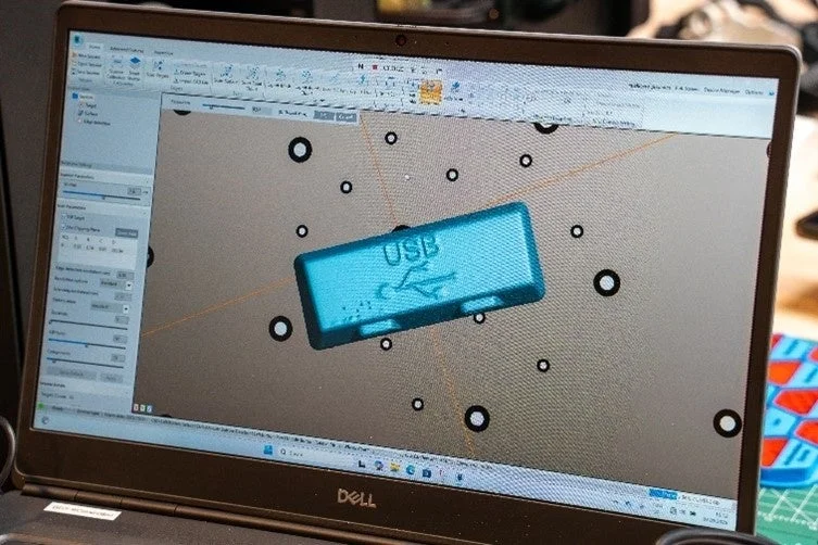 ノートパソコンの画面に3Dモデリングソフトウェアが表示されており、USBロゴが刻印された青いUSBドライブのモデルが中央に描かれています