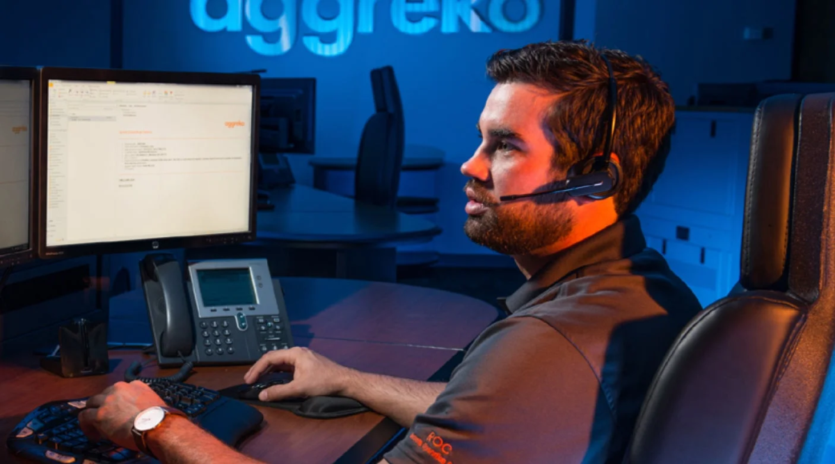 ヘッドセットを装着した男性が、薄暗いオフィスでコンピューターを使って作業しています