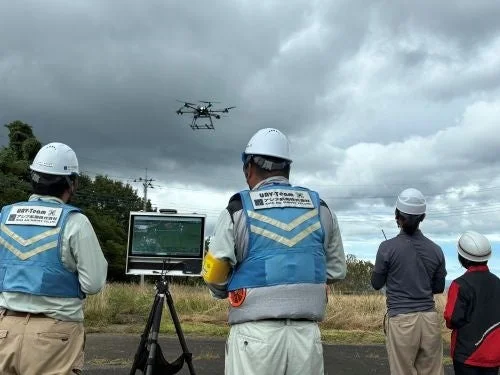 屋外で安全ヘルメットとベストを着用した作業員たちがドローンを操作している