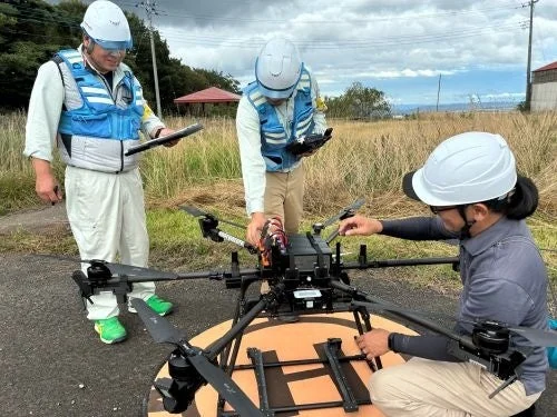 屋外で3人の作業員が大型ドローンの準備や点検を行っています