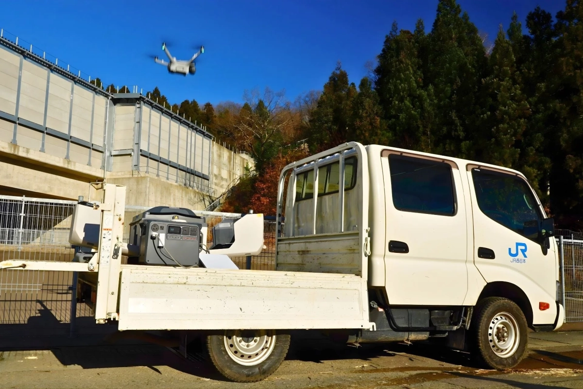 JR西日本のトラックの荷台にポータブル電源が積まれ、上空にはドローンが飛行しています。