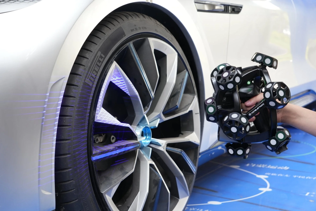 白い車のタイヤとホイールを3Dスキャンデバイスで測定している様子