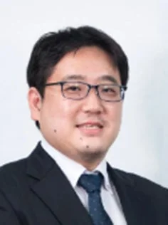 スーツと眼鏡を着用し、笑顔を見せるアジア人男性の胸から上の肖像写真