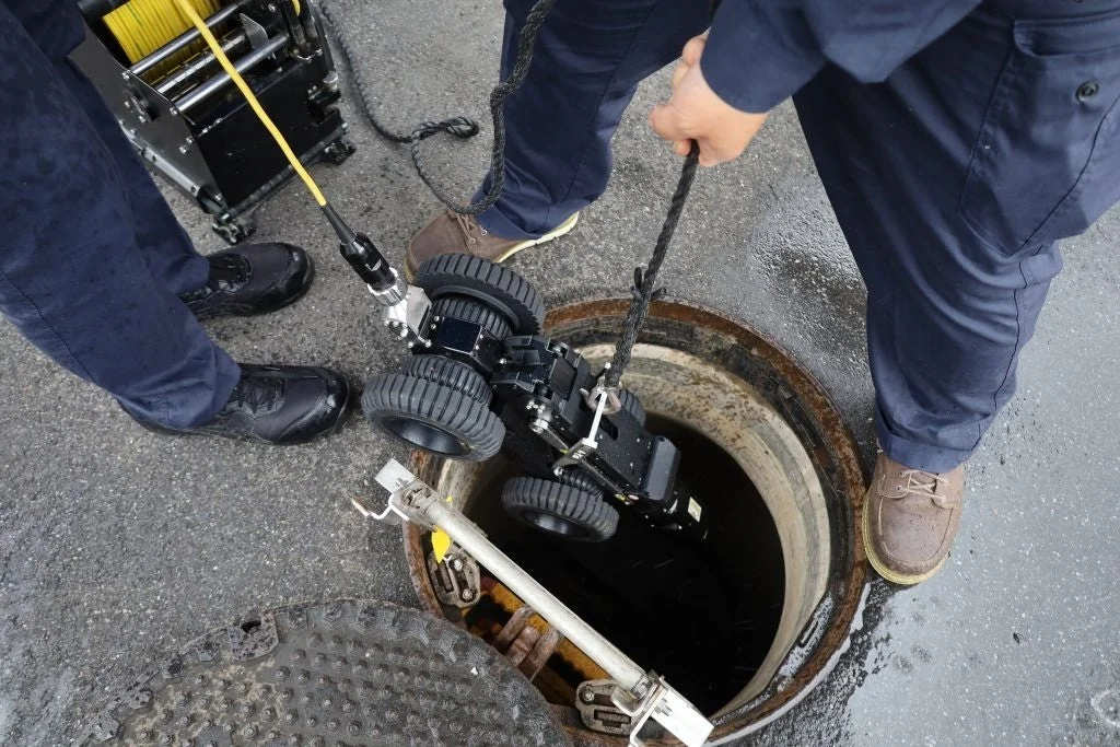ロボットをマンホールに降ろす作業員