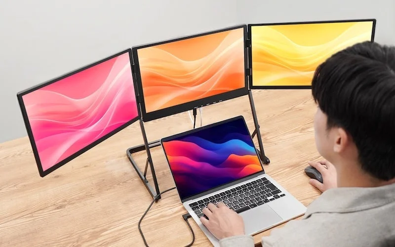 ノートパソコンに3つの外部モニターを接続し、トリプルディスプレイ環境で作業している人物の様子。広々とした画面で効率的に作業できるワークスペースが表現されています。