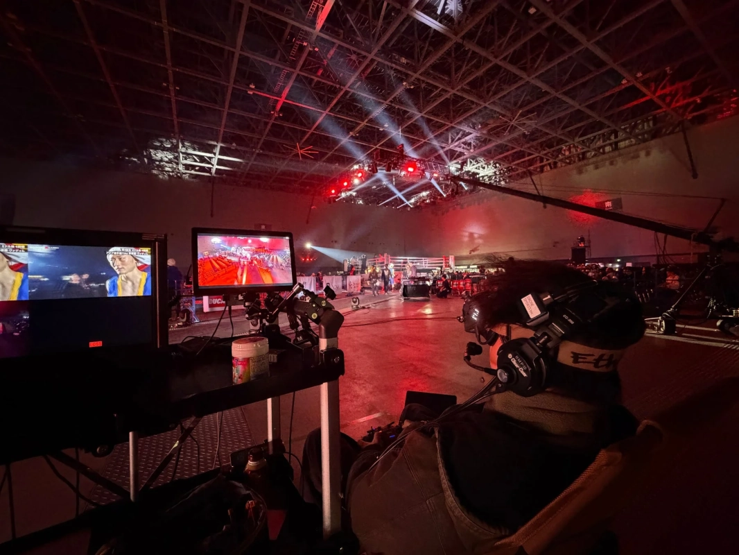 格闘技イベントの会場で、オペレーターがヘッドセットを装着し、複数のモニターで試合の様子を確認しながら中継作業を行っている舞台裏の様子