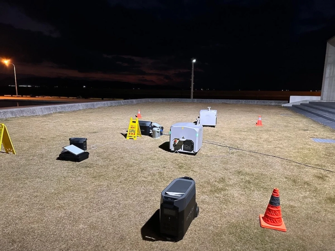 夜間の屋外の草地で、複数の測定機器やポータブル電源が設置されている