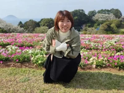 カラフルな花畑の前でしゃがみこみ、笑顔を見せる女性のポートレート