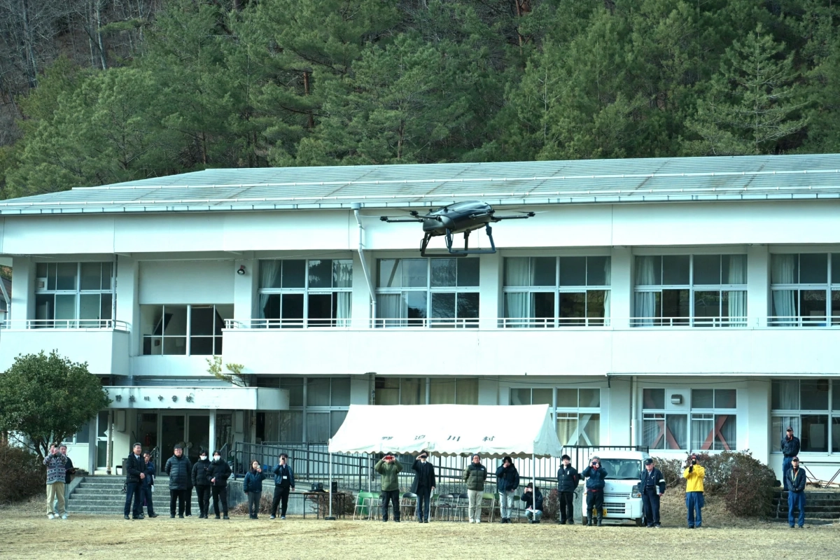 学校の校舎前で飛行するドローンと見上げる人々
