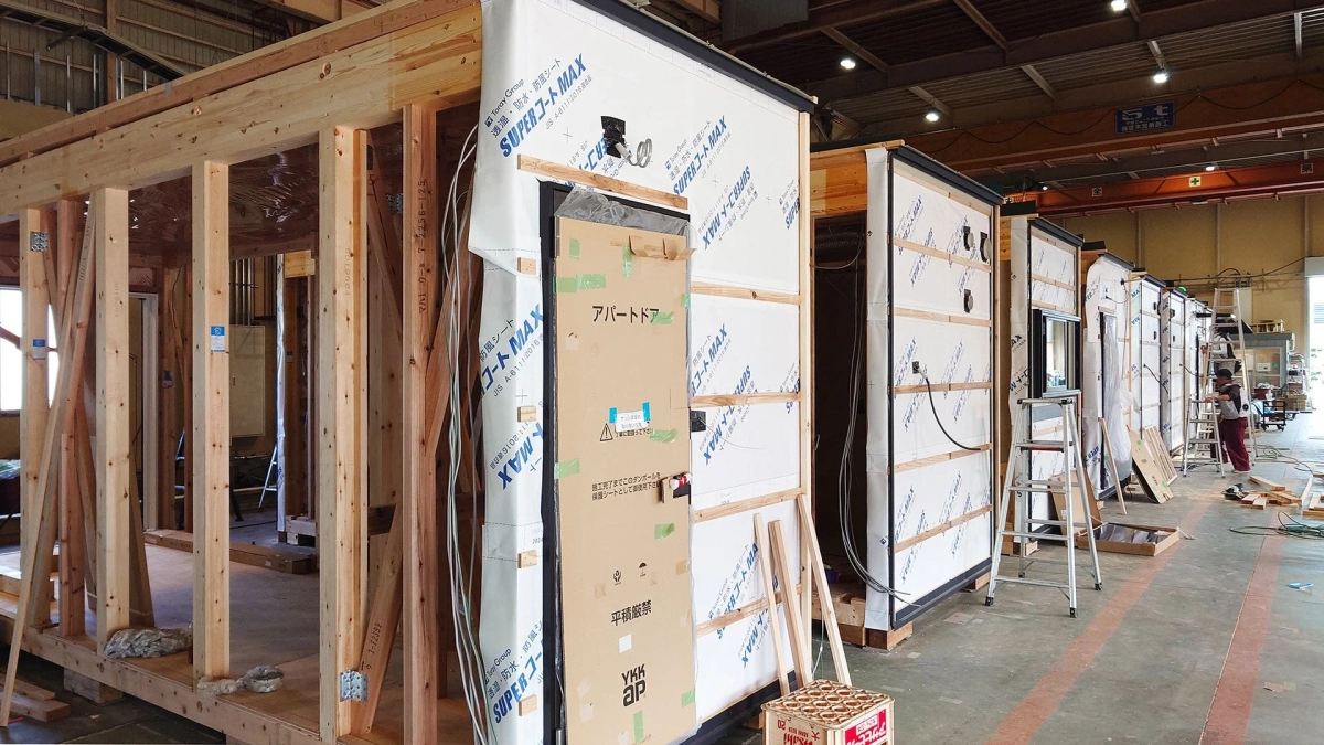 工場のような空間で複数のプレハブ住宅やアパートの建設モジュールが並べられ、工事が進められている様子