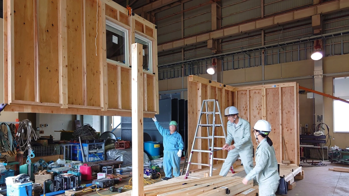 工場内で複数の作業員が木造建築のモジュールを組み立てている様子
