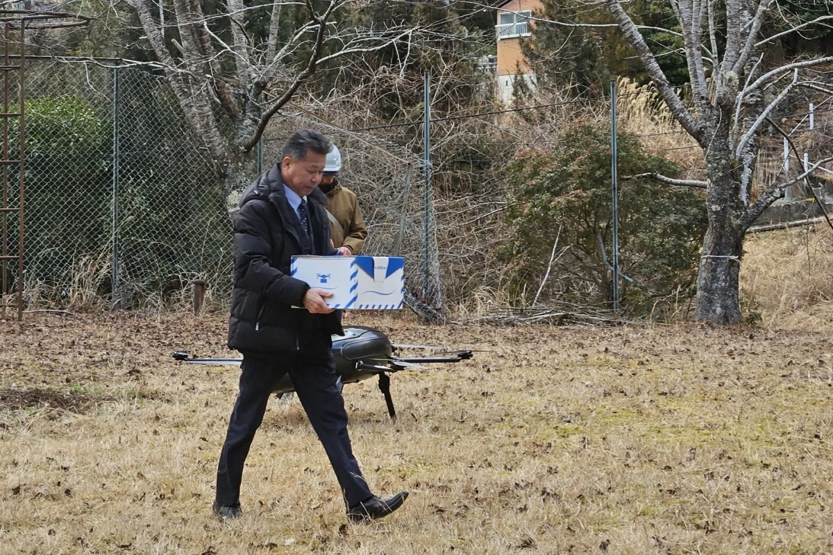 ドローンが置かれた草地で、配送された白いパッケージを持つ男性