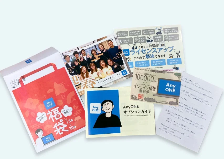 AnyONE関連の複数の販促物や資料が並べられています。これには、福袋、ライセンスアップの案内、10万円相当のオンライン講習無料券、オプションガイド、社員写真などが含まれ、企業向けのサービス利用促進や情報共有の課題解決を目的とした内容です。