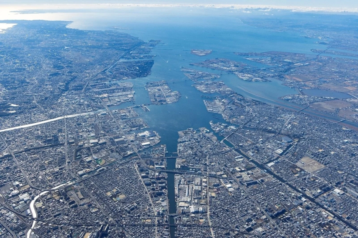 広大な都市が湾岸地域に広がり、多くの人工島や工業施設、複雑な水路と道路網が見える航空写真