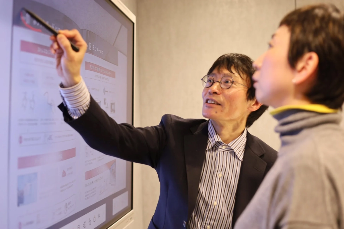 ビジネスシーンで男性が大型モニターを指し示している