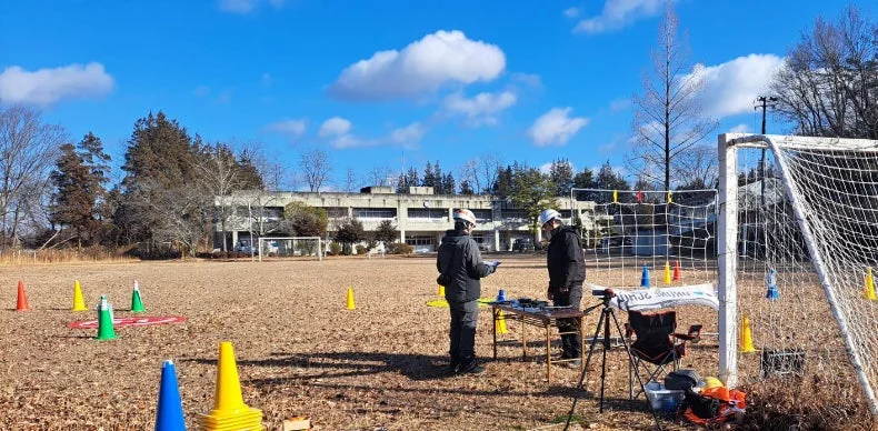 広いグラウンドで2人の作業員がドローン訓練を行っている様子