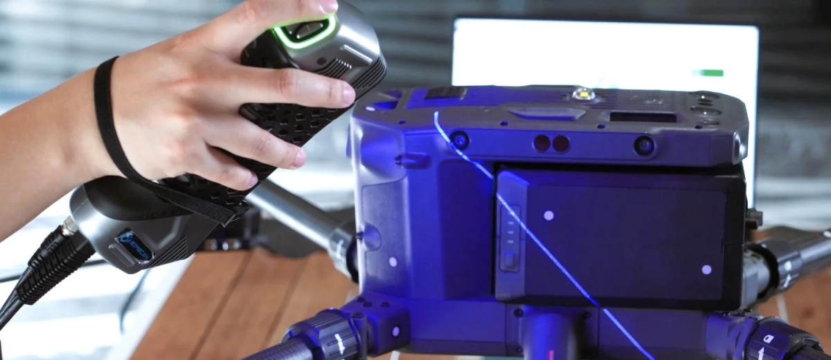 手持ちの3Dスキャナーのようなデバイスが、青いレーザー光を放つ大型機器に向けて操作されている様子