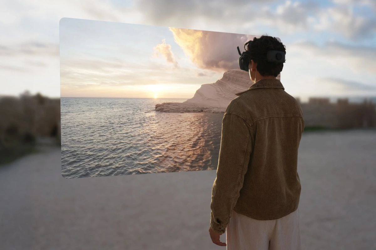 VRヘッドセットを装着した人物がビーチに立ち、目の前に広がる仮想スクリーンで美しい夕焼けの海と白い崖の景色を眺めている。