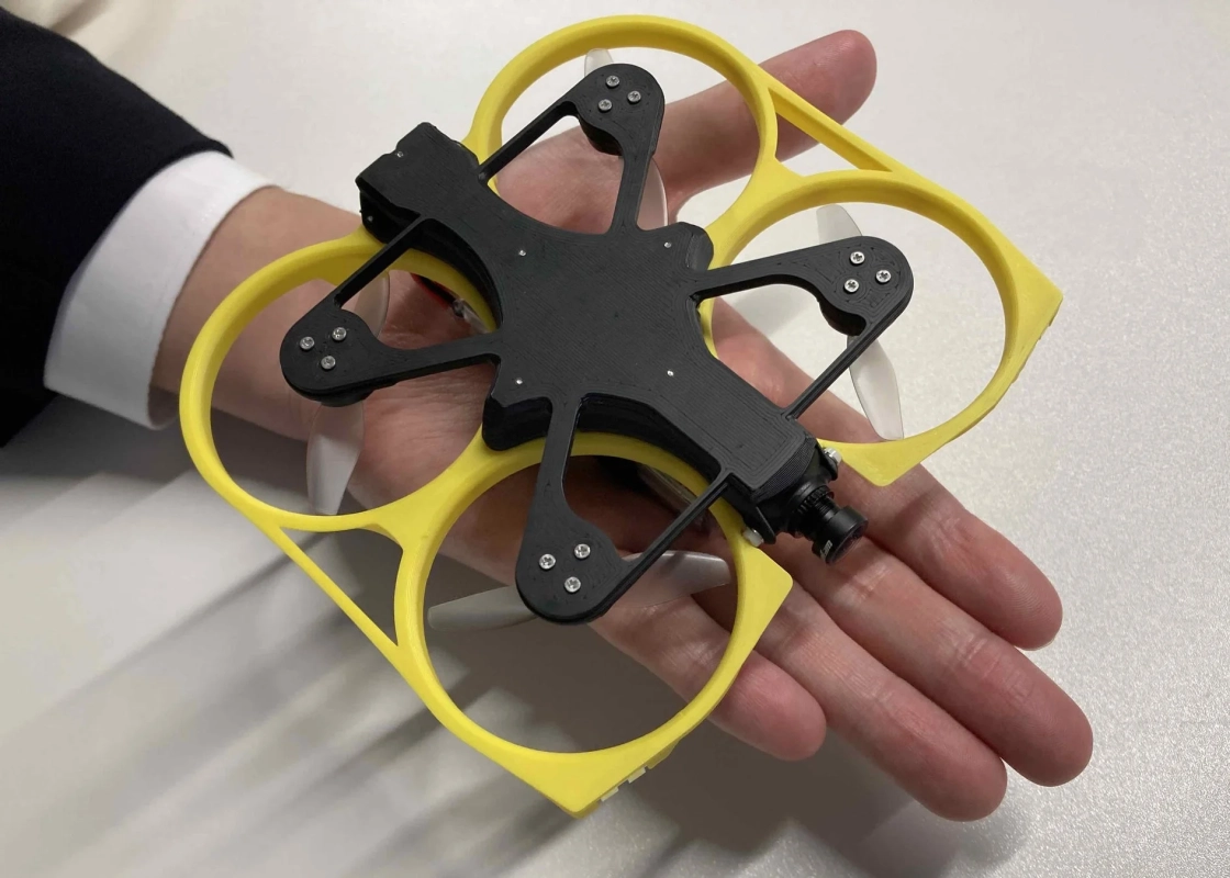 手のひらに収まるサイズの小型ドローンが写っています。黄色いプロペラガードと黒い本体が特徴で、前面にはカメラが搭載されています。