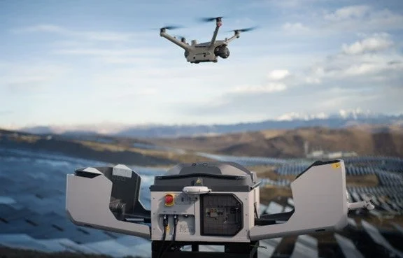 広大な太陽光発電所を背景に、ドローンが自動充電ステーションの上空を飛行