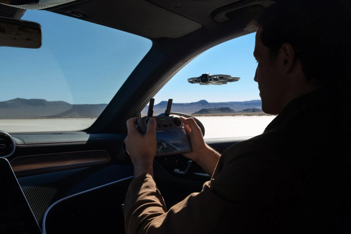 広大な砂漠の風景の中、車内から男性がドローンを操作している様子。