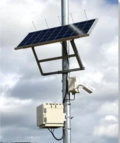 太陽光パネルが設置されたポールに監視カメラのようなデバイスと白い制御ボックスが取り付けられている様子