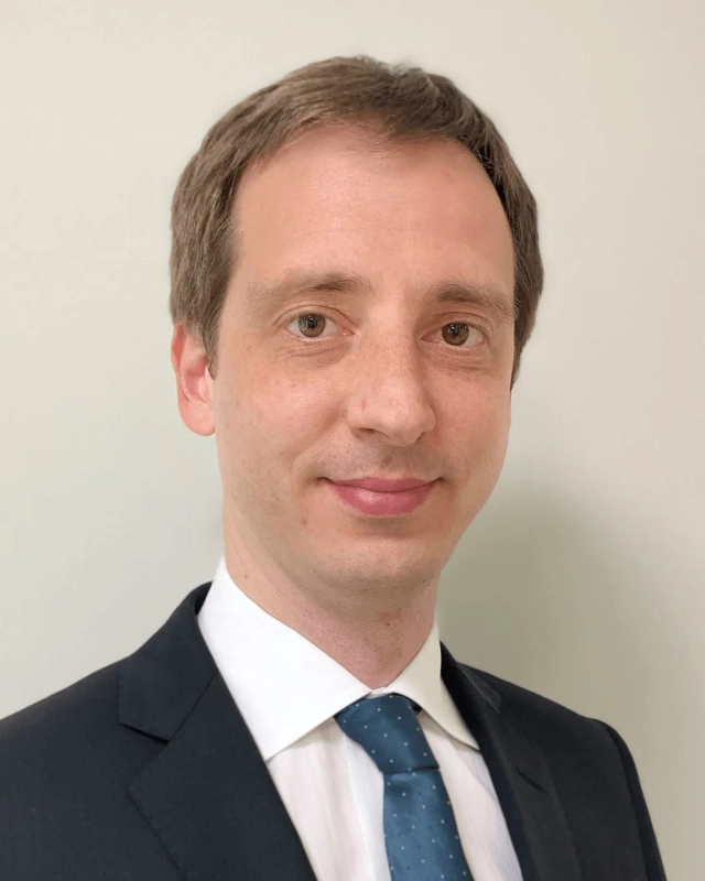 白い背景の前で、ダークスーツと青いドット柄ネクタイを着用した男性のプロフェッショナルなポートレート