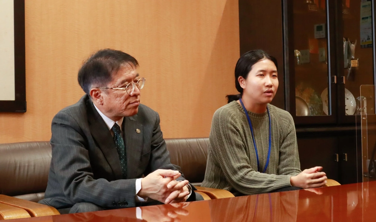 スーツ姿の男性とセーターを着た女性がテーブルに座り、真剣な表情で話し合っている様子。室内での会議か対談の場面と見られる。