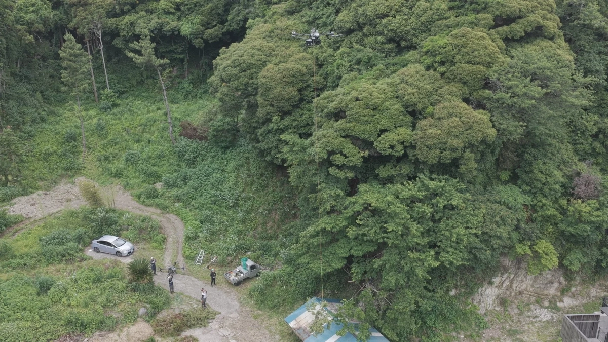 森林に囲まれた山間部でドローンが飛行している様子