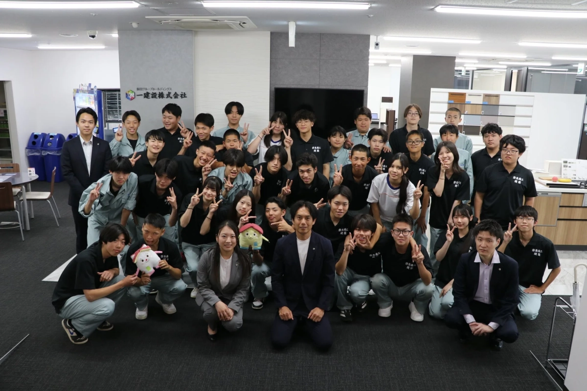 建設会社のオフィスで、多数の学生と数名の社会人が集合写真を撮っている様子