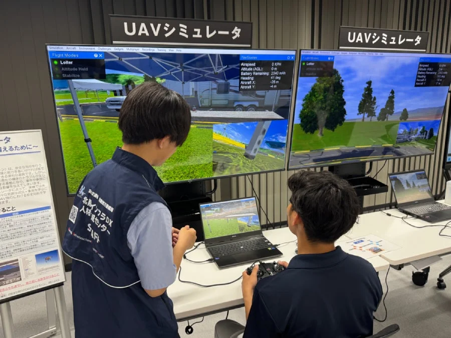 UAVシミュレーターを使ってドローンの操作を学ぶ二人の様子。