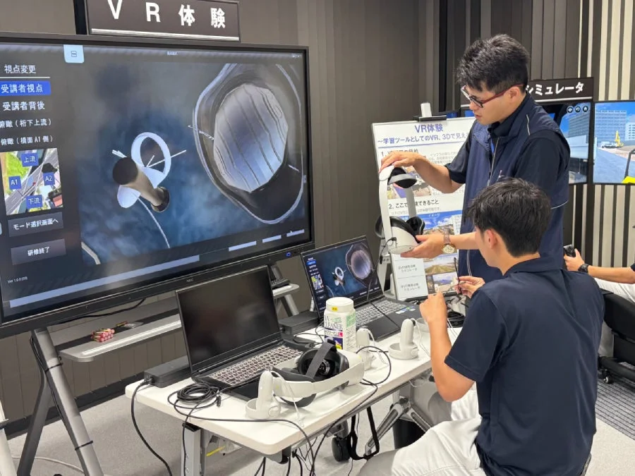 VRヘッドセットを装着した男性が仮想現実体験をしている様子。大画面にはVRシミュレーション画面が表示されている。