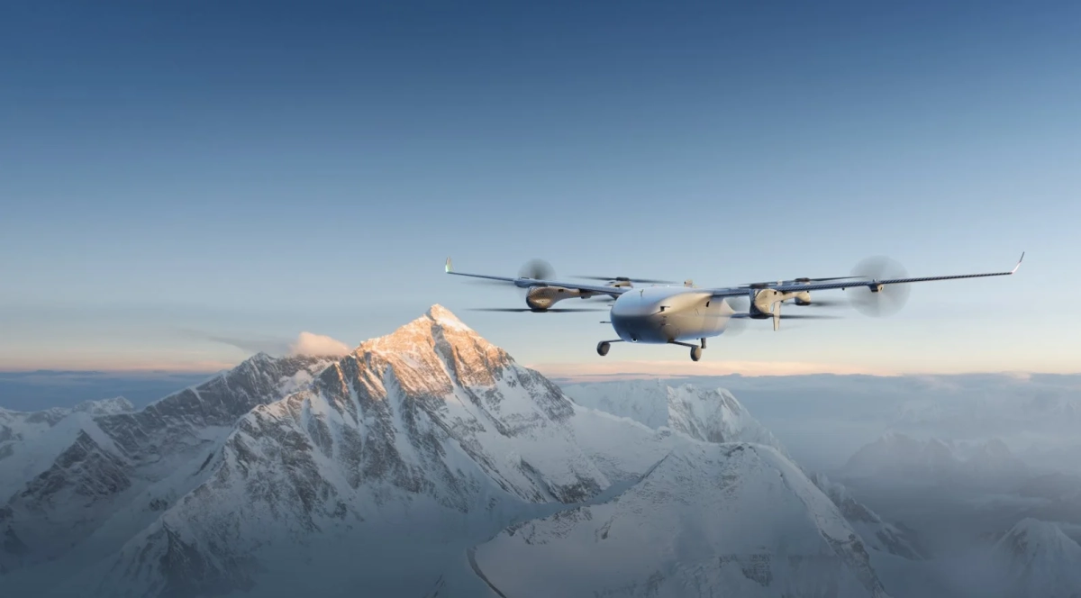 雪に覆われた雄大な山々の上空を、先進的なドローン型航空機が飛行している様子を捉えた画像です。山頂は朝焼けか夕焼けで金色に輝き、澄み切った青空が広がっています。