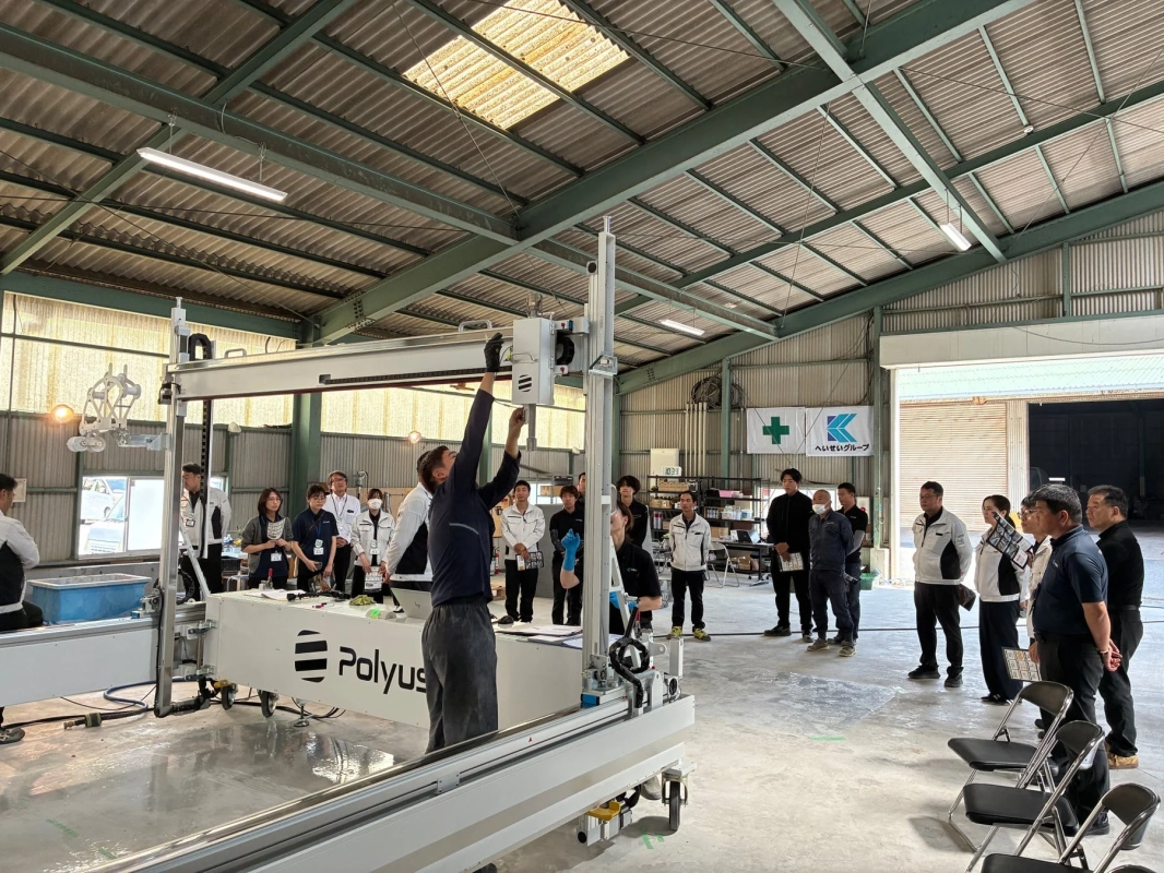 広々とした工場内で、多くの人々が大型機械のデモンストレーションや研修に参加している様子