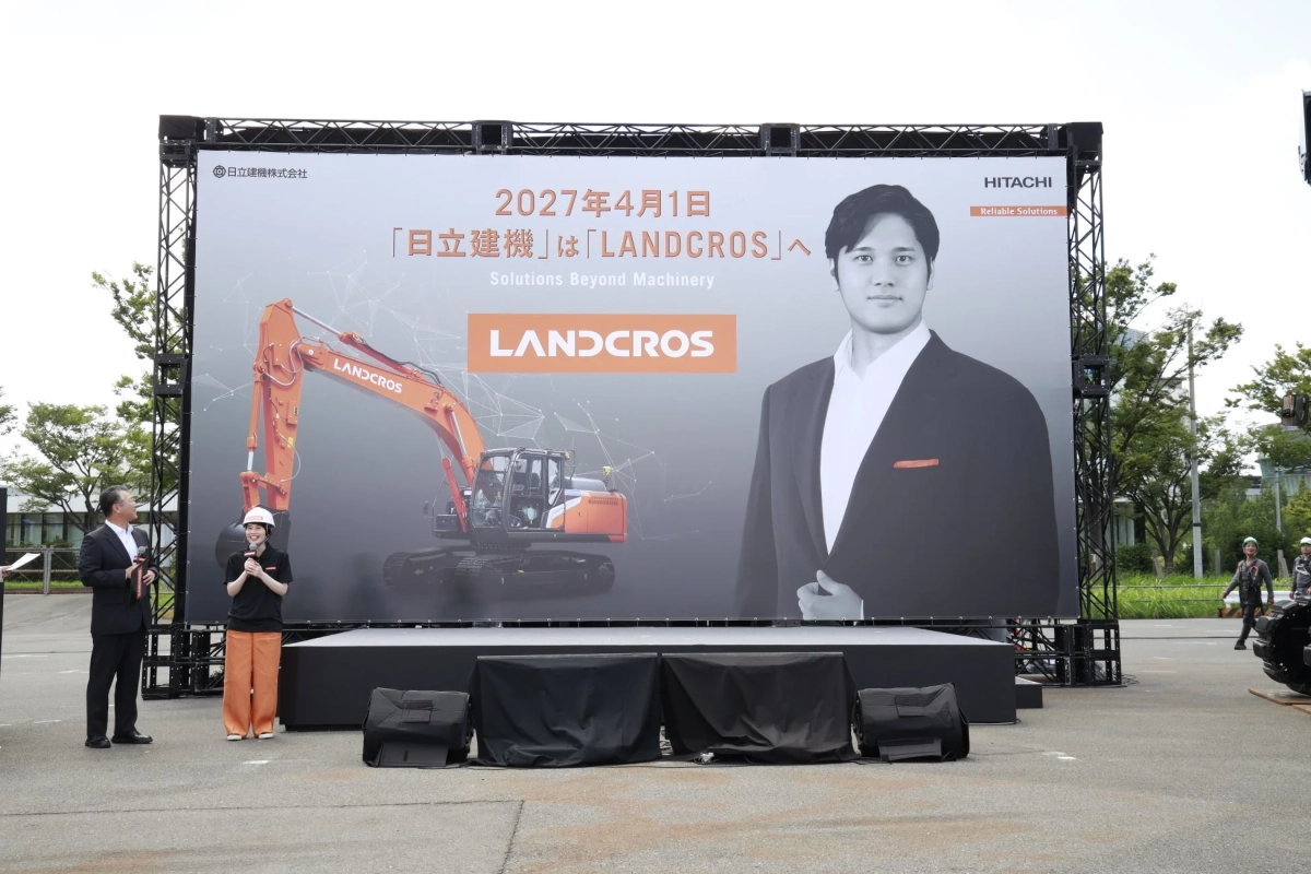 日立建機が2027年4月1日からの新ブランド「LANDCROS」への変更を発表する屋外イベントの様子です。大画面には大谷翔平のポートレートとオレンジ色の掘削機が映し出されており、ステージ上では関係者がマイクを持って話しています。