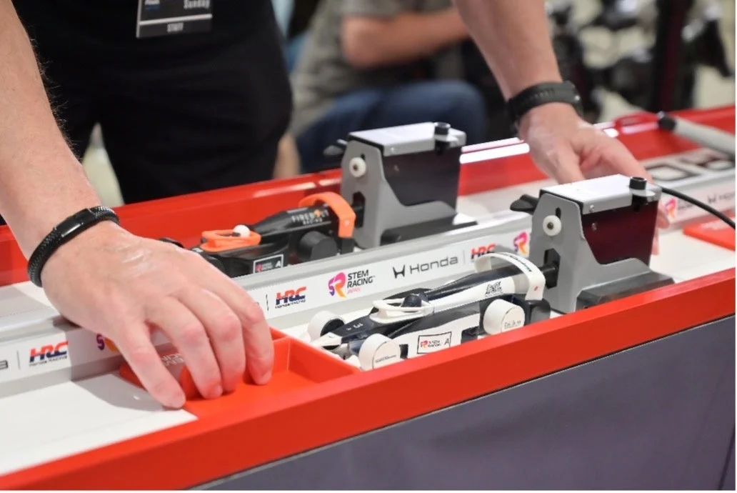 ホンダがスポンサーするSTEMレーシングイベントで、参加者がミニチュアのレーシングカーをコースにセットしている様子