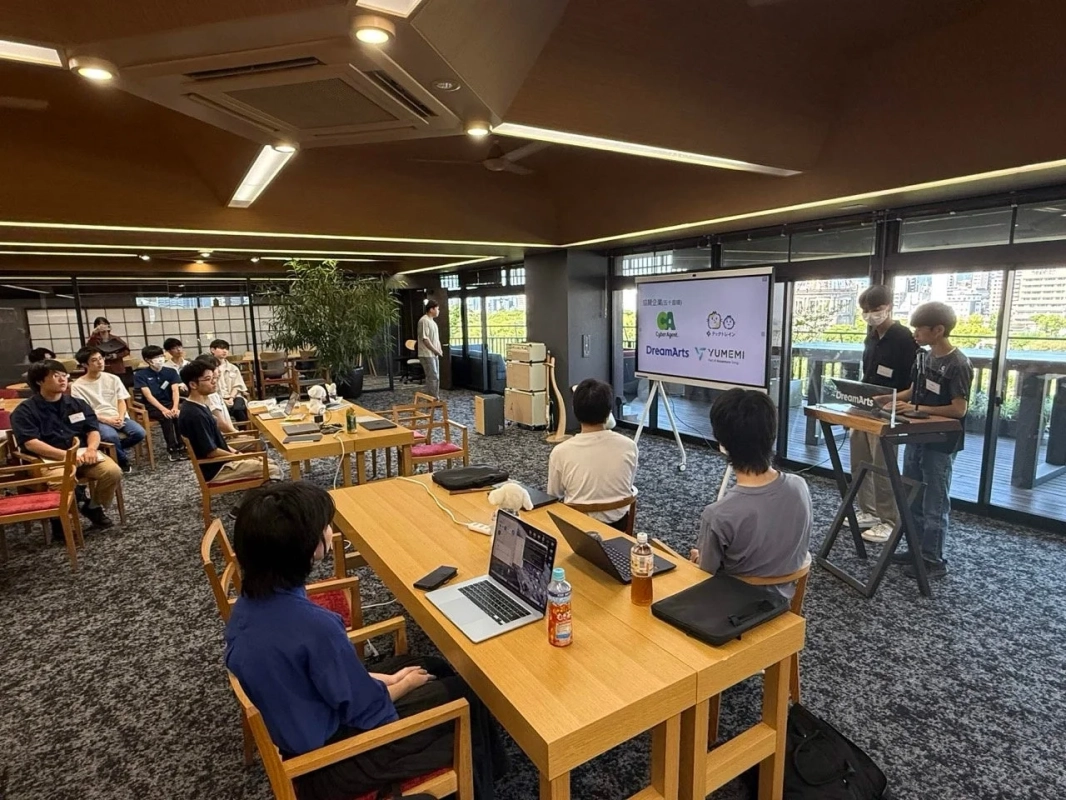 企業ロゴが映し出されたスクリーンを見る若者たち