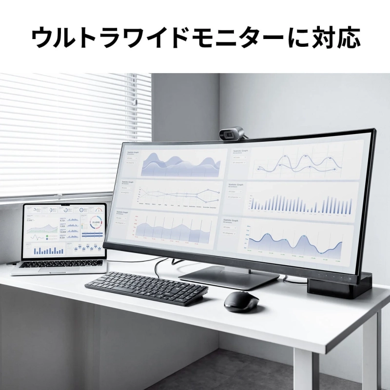 ウルトラワイドモニターとノートパソコンが並べられた、データ分析画面を表示するモダンなオフィスデスクの様子