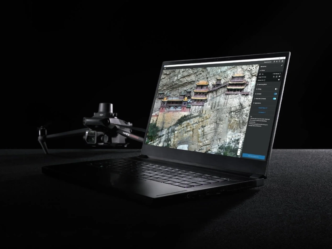 暗い背景に置かれたノートパソコンが崖の上の寺院の3Dモデルを表示しており、その手前にはDJI Mavic 3ドローンが写っています。ドローンを用いた測量や3Dモデリング作業を示す画像です。