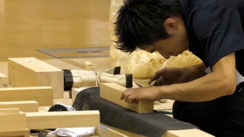 工房で職人が木材らしき素材を丁寧に加工している様子